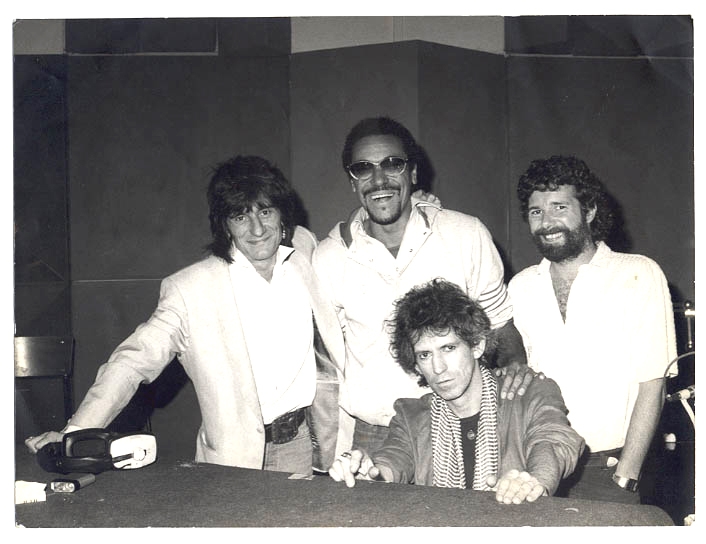 Na foto, que é em preto e branco , Marku Ribas posa ao lado de três integrantes da banda Rolling Sones. Três posam de pén enquanto um permanece sentado. 